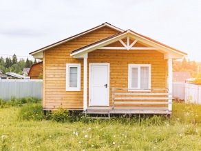 Small tiny wooden frame house with sundeck and white windows and door as a country residence in sunny summer day.